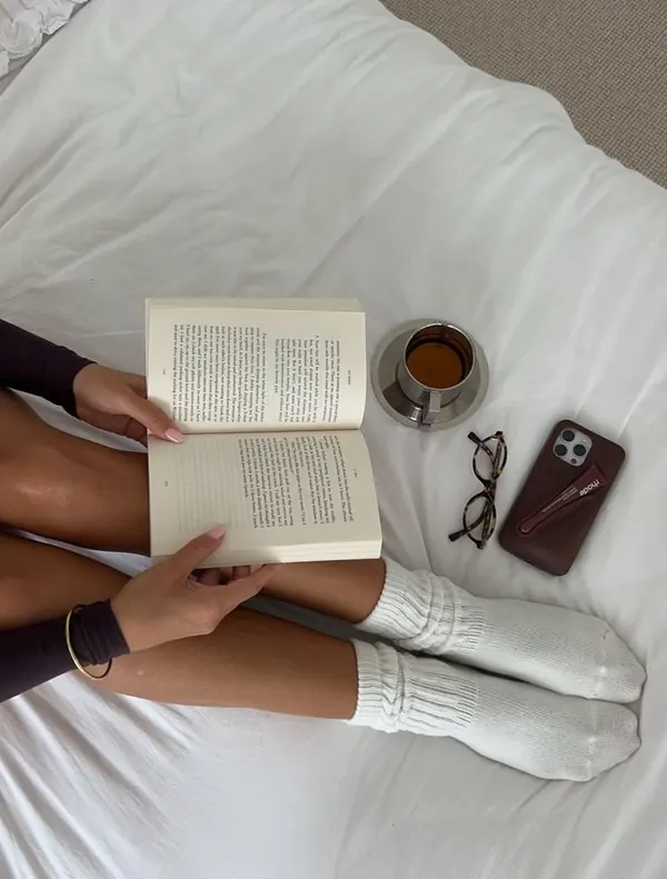 Livro aberto, chá e óculos sobre a cama